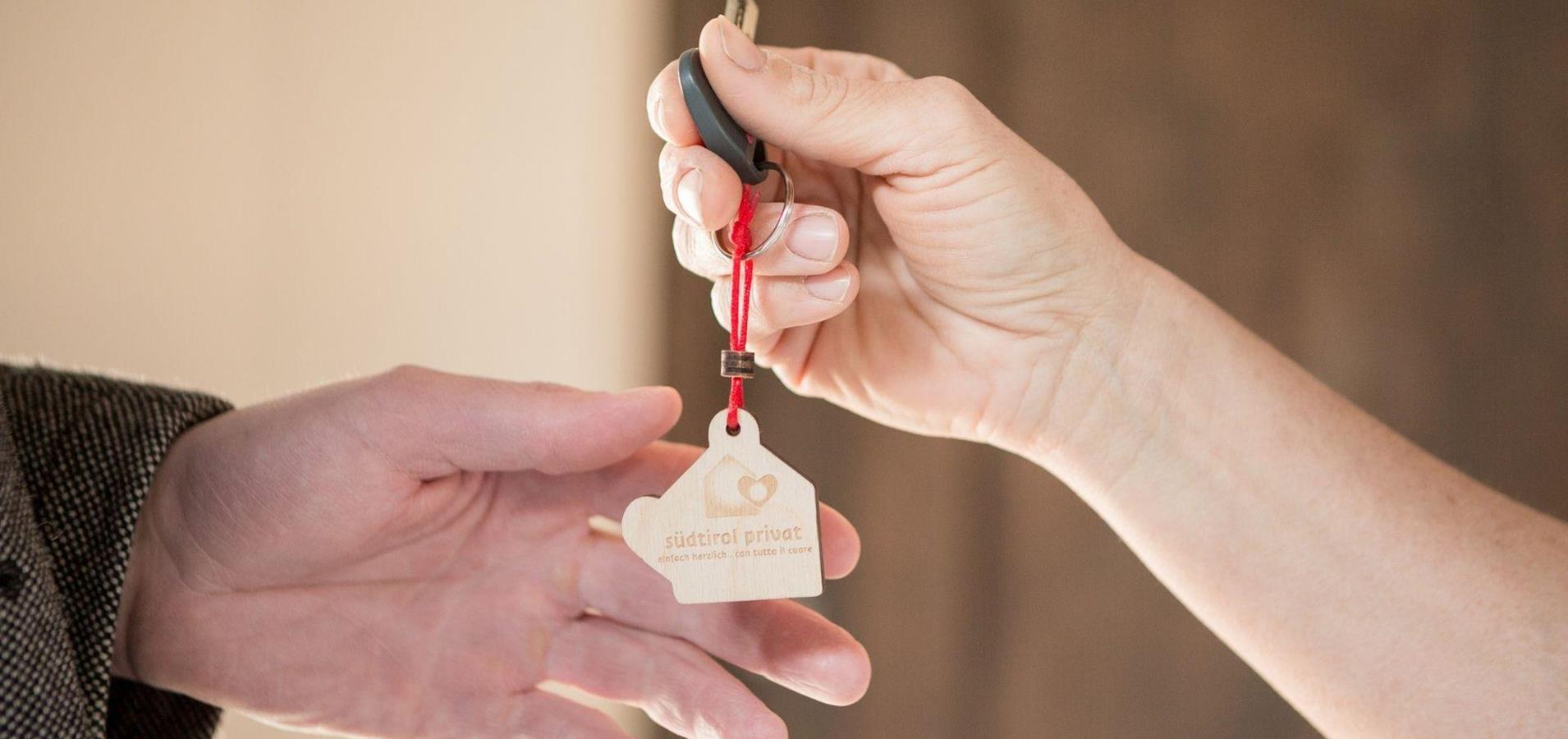Close-up of handing over keys with a wooden “südtirol privat” keychain between two hands.